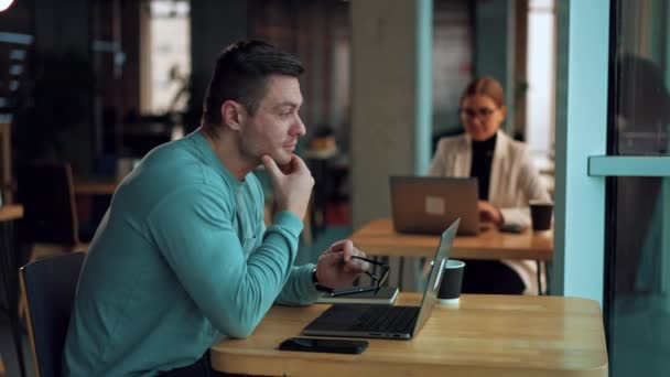 一个疲惫的人坐在笔记本电脑前揉揉眼睛 手里拿着眼镜 商人戴上眼镜 继续在电脑上工作 女士在笔记本电脑前工作 背景模糊不清 — 图库视频影像