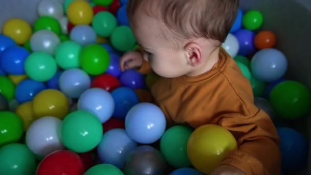 Kleinkind Orangefarbenem Hemd Sitzt Weichen Becken Zwischen Den Bunten Bällen — Stockvideo