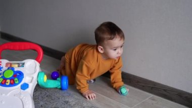 Turuncu spor takım elbiseli güzel erkek bebek elinde bir emzik tutarak yerde sürünüyor. Sevimli çocuk arzulanan oyuncağa ulaşmaya çalışıyor.