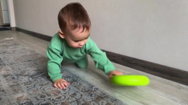 Sürünen sevimli bebek elinde plastik bir yüzük taşıyor. Israrcı küçük çocuk yukarı oyuncak almaya gidiyor..