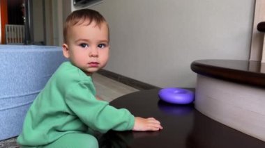Güzel, beyaz, gri gözlü bebek içeride, yerde oynuyor. Siyah evcil kedi arkada görünür ama çocuk bunu fark etmez. Kapat..