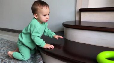 Sevimli küçük çocuk oyuncağı atar ve merdivenlerde onu takip eder. Güzel çocuk basamakları tırmanıyor ve iki kez hapşırıyor..
