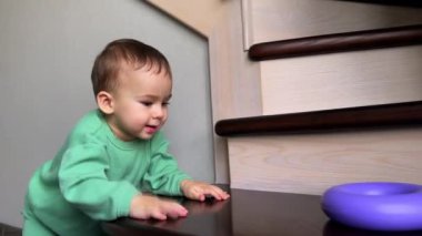 Merdivenlerde oyuncağıyla oynayan tatlı bir bebek. Bebek plastik yüzüğü basamağa atıyor ve geri almak için takip ediyor..