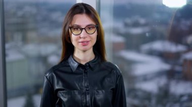 Gülümseyen koyu renk saçlı bayan gözlüklerini çıkarıyor. Kadın yüzünü pencereye çevirir ve manzaraya bakar..