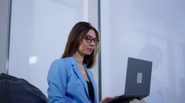 Gözlüklü kadın laptoptaki işiyle meşgul. Kucağında tutmak için alet kullanan bir kadın. Düşük açı görünümü.