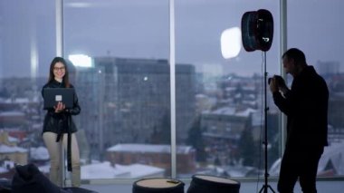 Kameraman elinde dizüstü bilgisayar olan bir kadının fotoğrafını çekiyor. Manken elinde aletle panoramik pencerenin önünde duruyor. Bulanık arkaplan.