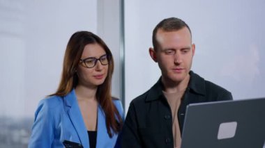 Kafkasyalı meslektaşlar dizüstü bilgisayardan video izliyorlar. Adam bilgisayarı pencerede tutuyor ve kadının elinde telefon var..