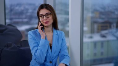 Mavi ceketli güzel bayan pencerede oturuyor. Telefondaki kadın gülümsüyor. Bulanık arkaplan.