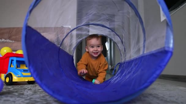 プラスチックのおもちゃのトンネルでクロールする幸せな陽気な赤ちゃんの少年 自宅で遊ぶ愛らしいトッドラーは 彼の太鼓を手に持っています — ストック動画