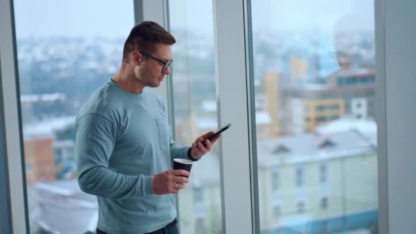 戴眼镜的严肃男人凝视着手机屏幕 在办公室里使用智能手机和喝咖啡的商人 — 图库视频影像