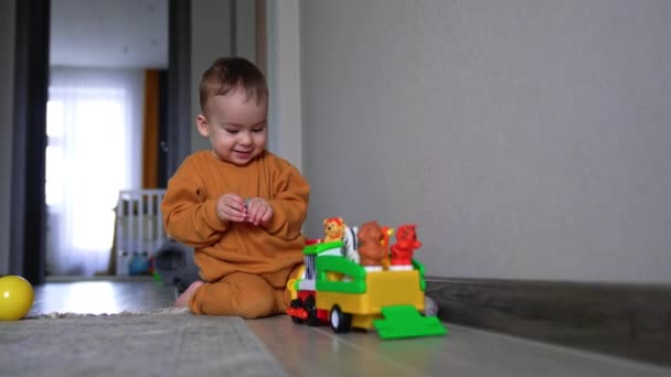 かわいい赤ん坊は床に座り ローリーが近づいてくるのを見ながら微笑んでいる 手のひらを押し おもちゃの上に回すおしゃぶりを持つ子供 — ストック動画