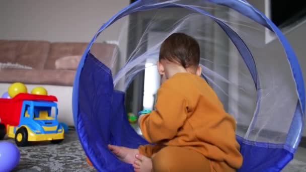 美しい赤ちゃんは部屋の床にあるトンネルに座っています 屋内でアクティブなゲームのための時間を持っている白人子供 — ストック動画