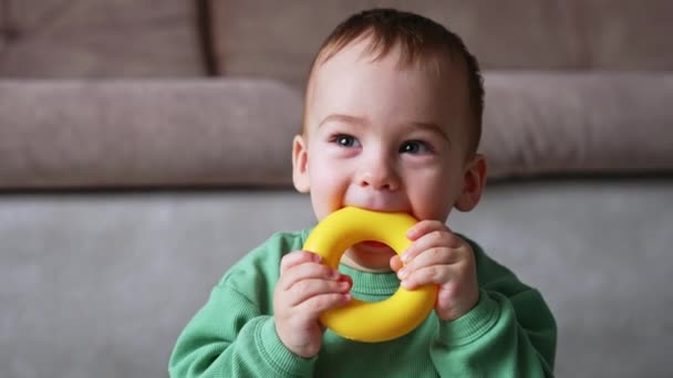 有趣的可爱的孩子尝他的塑料玩具 一个可爱的婴儿在家里玩玩具的肖像 靠近点模糊的背景 — 图库视频影像