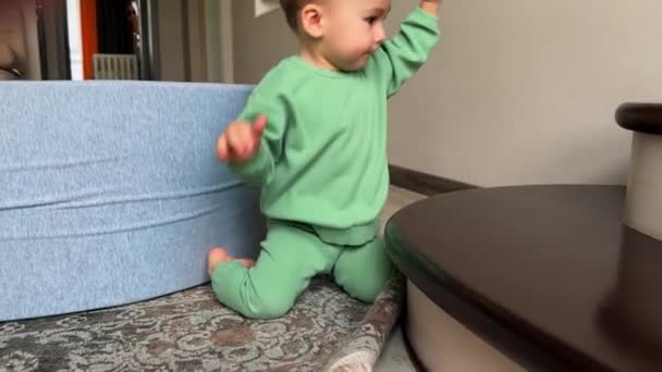 緑のスポーツスーツの1歳のトッドラーは階段の近くで屋内で演奏しています 甘い子供はおもちゃを投げて それが落ちるか回転するのを見ます — ストック動画