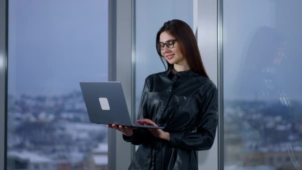 穿着黑色衬衫的女人使用现代技术 女士站在窗前用笔记本电脑工作 布鲁内特完成了工作 看着窗户 — 图库视频影像