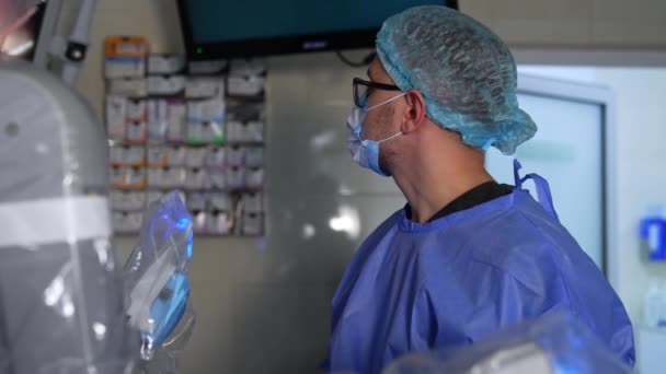 戴眼镜的白人男性医生监测机器人设备的工作 医生的画像集中在手术室的屏幕上 侧视图 — 图库视频影像