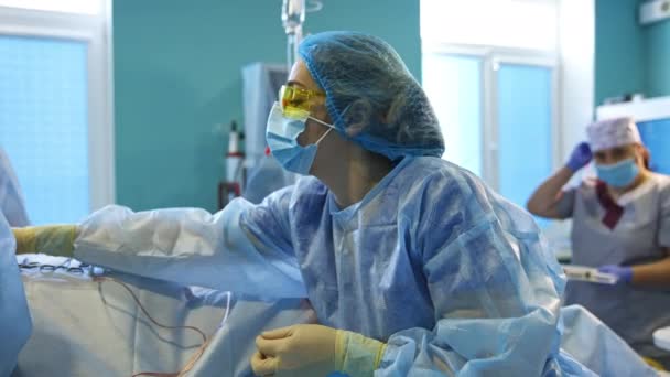 手術中の外科医チームを支援する女性医師 黄色い眼鏡の看護師はスポンジを準備し それらを渡します — ストック動画