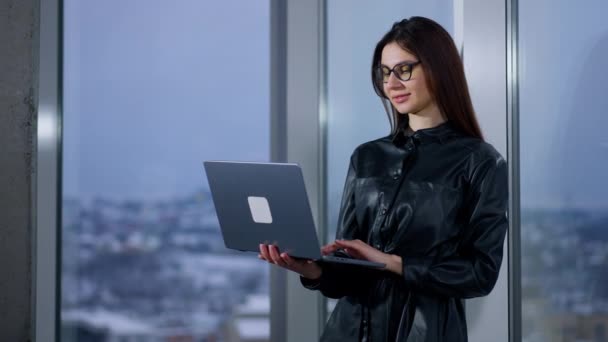 ラップトップにメガネをかけている若い女性ビジネスパーソンは 手に持っている 女性は仕事を終え コンピュータを閉じ 窓を見るために回ります — ストック動画