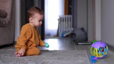 Elinde emzik olan tatlı bir çocuk yerde oturup topa bakıyor. Küçük çocuk oyuncağa yaklaşıyor ve onu itiyor, yuvarlanışını izliyor..