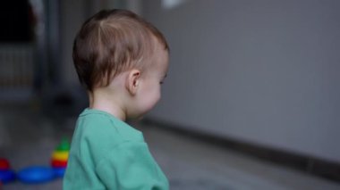 Küçük bebek içeride oturmuş, oyuncak yüzüğün yere yuvarlanmasını izliyor. Yan görüş. Çocuk oyuncağı alır ve fırlatır..