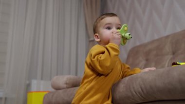 Güzel çocuk kanepeye yaslanmış ağzına bir oyuncak tutuyordu. Bir yaşında dişleri büyüyen bir bebek oyuncağıyla onları tırmalıyor..