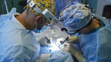 Doktorlar operasyon alanını kafalarında el fenerleriyle aydınlatıyorlar. İşbirliği yapan cerrahlar forseps kullanırlar. Yüksek açı görünümü.