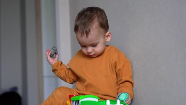 小男孩坐在地板上 专心致志地盯着玩具车 从车上取出人偶 孩子们在汽车接近时推它 — 图库视频影像