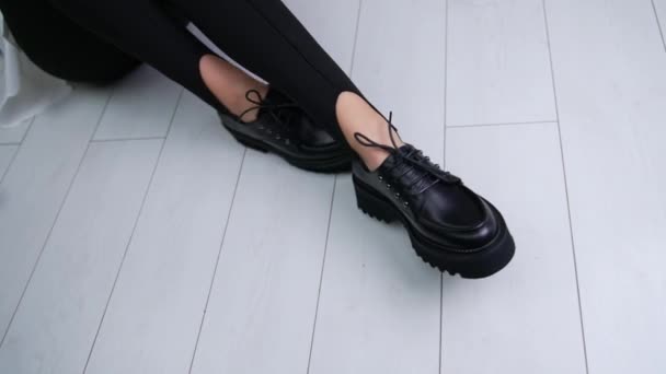 Lady Mendemonstrasikan Sepatu Hitam Dengan Tali Duduk Lantai Putih Wanita — Stok Video