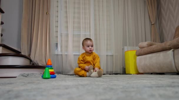 사랑스러운 아이는 거실에서 바닥에 앉아있다 누군가가 장난감 반지를 소년에게 굴리고 — 비디오