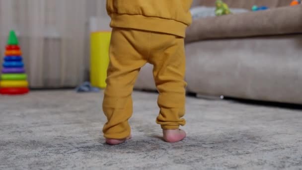 身穿橙色运动服的孩子正在学习如何在室内行走 婴儿在妈妈的支持下迈着脚高的步伐 — 图库视频影像