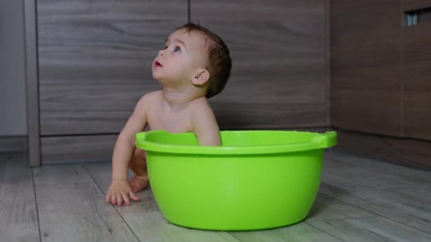 裸の小さなトッドラーが屋内の緑の浴槽の後ろに座っています 子供は喜んでウォッシュボールから水を飛ばします — ストック動画
