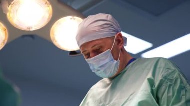 Kıdemli cerrah ameliyat edilen hastaya bir an için başını çevirir. İşine odaklanmış odaklanmış bir doktorun portresi..