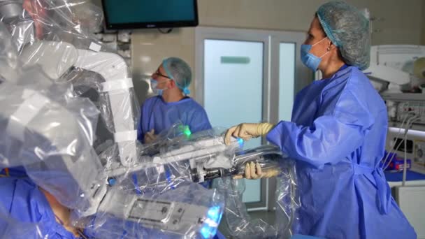 ロボットアームを握るダ ヴィンチロボットのオペレーションフィールドに立っている女性医師 医者はスクリーンを見ている腕を動かし 別の腕を取ります — ストック動画