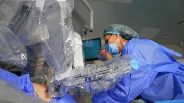 ロボット操作装置アームは患者の腹部に移動する 機械による最小侵入作戦 バックドロップで医師と看護師 — ストック動画
