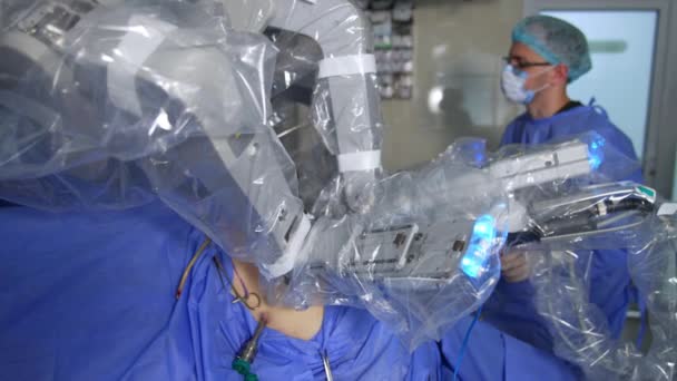 現代手術室で人間を操作するハイテクロボット 眼鏡の男性外科医がロボットの近くに立ってプロセスを監視 — ストック動画