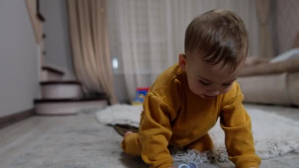 小さな赤ん坊が床に座って おしゃぶりを口にした 子供はソーザーを緩め それを拾い上げて口に引っ張る — ストック動画