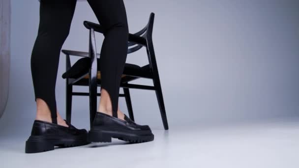 トラクターソルで黒い靴を履いた女性モデルウォーク 女性はスタジオの椅子の近くを歩く黒い靴を示しています クローズアップ — ストック動画