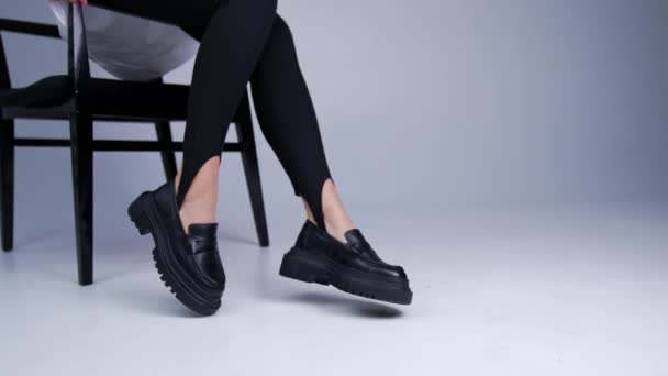 穿着黑腿和白衬衫的不为人知的女人展示了她的现代鞋子 模特儿坐在椅子上摸着她黑色时髦的拖鞋 — 图库视频影像