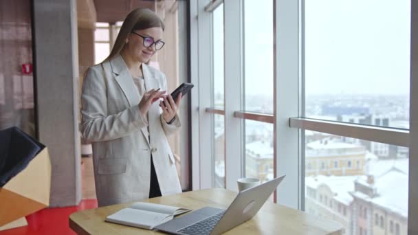 Kadını Elinde Telefonla Pencerenin Yanında Duruyor Ofis Çalışanı Bir Telefon — Stok video