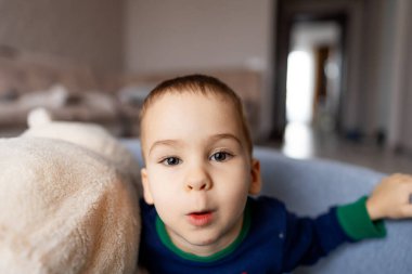 Sevimli küçük çocuk kanepede yatıyor ve komik bir yüz ifadesi takınıyor..