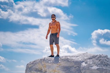 Kaslı adam gökyüzüne karşı bir kayanın üzerinde duruyor..