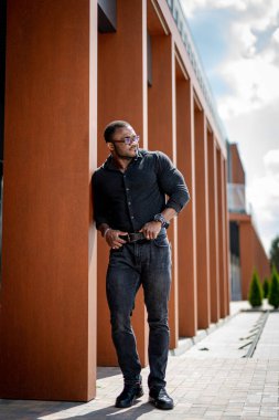 Genç yakışıklı Afro-Amerikalı adam şehirde dolaşıp kameraya poz veriyor. Şık bir adam şehirde dolaşıyor, şık bir adam şehirde dolaşıyor, genç ve yakışıklı Afro-Amerikan bir adam şehirde dolaşıyor ve kameraya poz veriyor. stylis