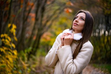 Sonbahar parkında beyaz ceketli güzel bir kadın sonbahar parkında yürüyor..