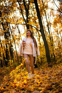 Genç kız elinde bir fincan kahveyle sonbahar parkında yürüyor. Genç kız elinde bir fincan kahveyle sonbahar parkında yürüyor..
