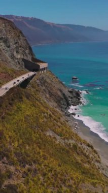 Kaliforniya kıyı şeridinde tünelleri olan iki şeritli otoyol. Kıyıdaki güzel gök mavisi okyanus manzarası. Üst Manzara. Dikey video.