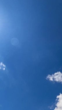 Mavi gökyüzünde parlayan parlak güneş. Güneşe doğru hızla uçan beyaz bulutlar. Aşağıdan bak. Zaman ayarlı. Dikey video.