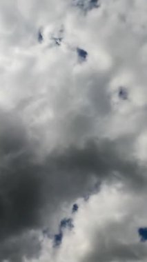 Mavi gökyüzünü tamamen kaplayan gri bulutlar. Parlak güneş bulutların arasından doğuyor. Zaman ayarlı. Dikey video.