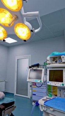Ameliyat masası hazırlandı ve ameliyat için hazırlandı. Modern cerrahi odasındaki boş odalarda gelişmiş lambalar yanıyor. Dikey video.