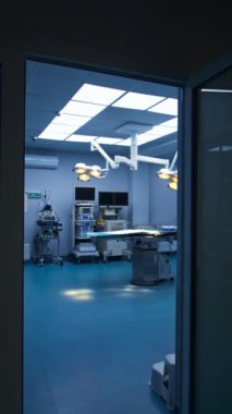 Karanlık bir koridordan aydınlık ve ferah ameliyathaneye girmek. Üzerinde lambalar açık bir şekilde operasyon masasına yaklaşıyoruz. Duvarda gelişmiş ekipmanlar var. Dikey video.