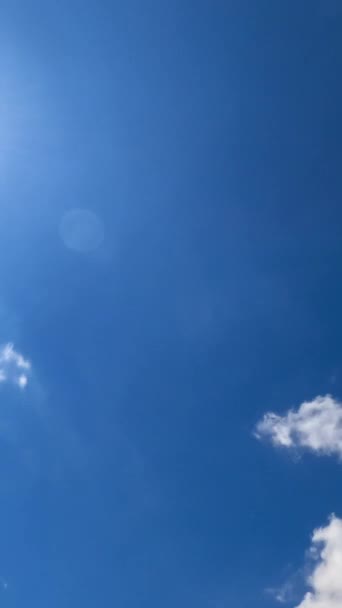青空に輝く明るい太陽 すぐに太陽に向かって白い雲を飛ぶ 下からの眺めです タイムラプス バーティカルビデオ — ストック動画